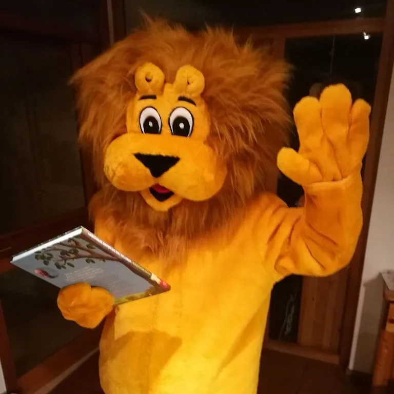 Löwe Leo hält ein Kinderbuch in der Pfote