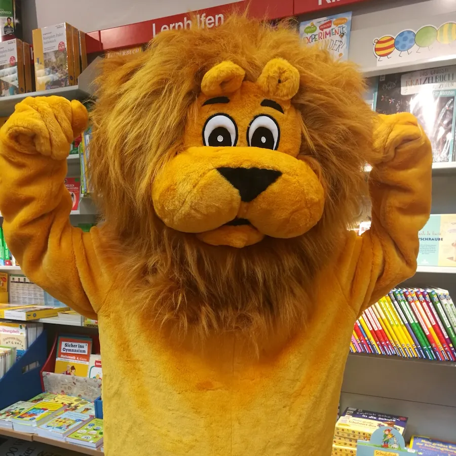 Löwe Leo reckt in einem Geschäft beide Arme in die Höhe