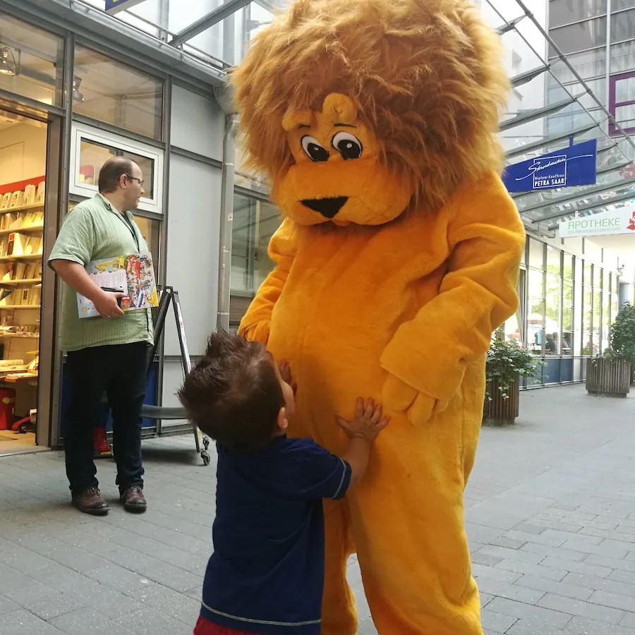 Kleiner Junge umarmt Löwe Leo in einer Fußgängerzone