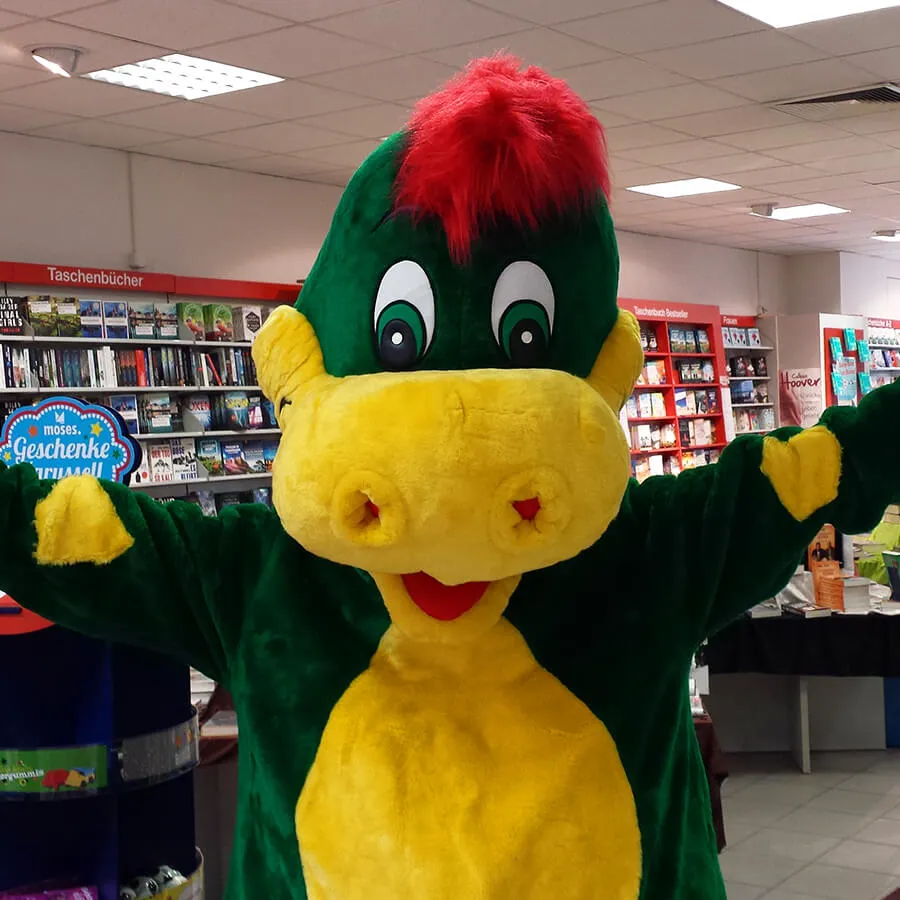 Drache Dinoli breitet in einer Buchhandlung die Arme aus